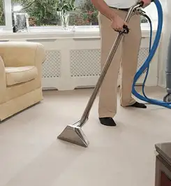 Professional carpet cleaner using a hot-water extraction wand and hose machine in a living room in Huntsville, AL.