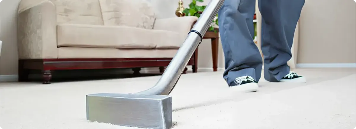 Carpet cleaning technician using a hot-water extraction wand on a light-colored carpet in a living room, Huntsville, AL.