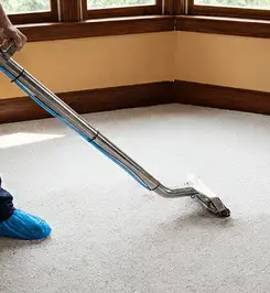 Steam carpet cleaning technician using a hot-water extraction wand on a residential carpet, wearing blue protective shoe covers Huntsville, AL.