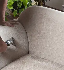 Professional upholstery cleaner deep-cleaning a fabric sofa with a handheld extraction tool and hose Huntsville, AL.