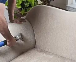 Professional upholstery cleaner deep-cleaning a fabric sofa with a handheld extraction tool and hose in Huntsville, AL.